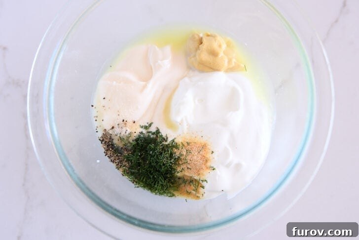 Glass bowl with mayo, greek yogurt, dijon mustard, dill, onion powder, black pepper and garlic powder.