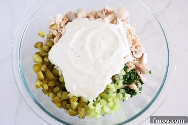 Glass bowl with celery, chopped dill pickles, green onions, chopped chicken and creamy dressing.