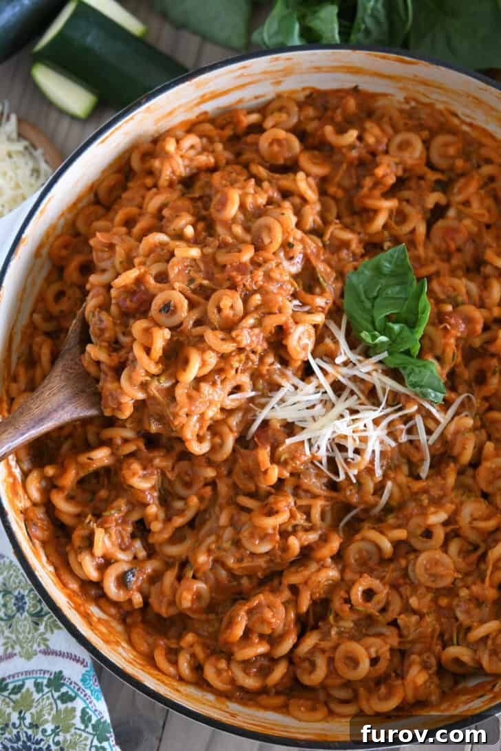Serving spoon scooping up helping of saucy pasta out of deep skillet.