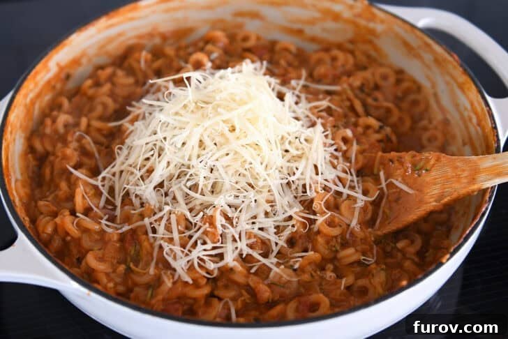 Adding freshly grated Parmesan to cooked pasta in red sauce with shredded zucchini in deep skillet.