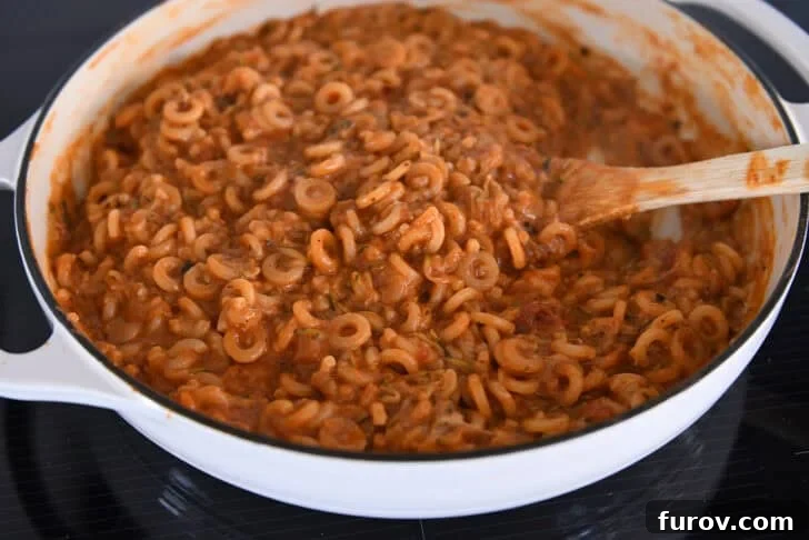 Cooking pasta in red sauce with shredded zucchini in deep skillet.