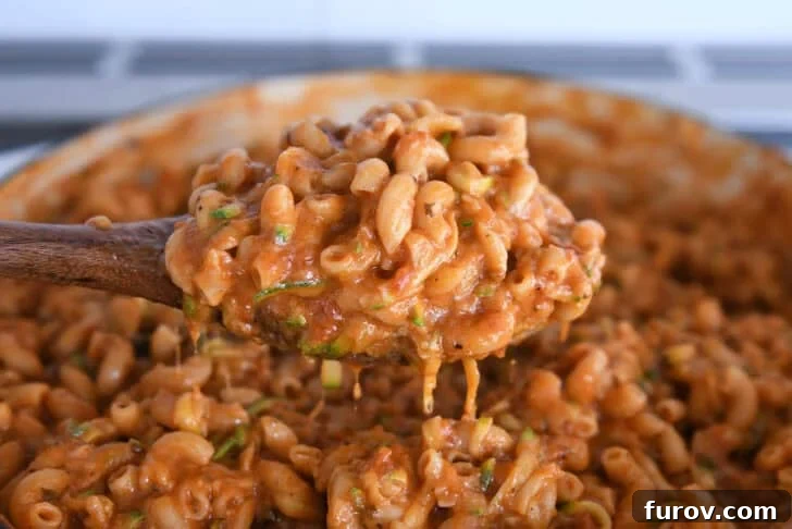 Spoon scooping up serving of saucy pasta with shredded zucchini in skillet.