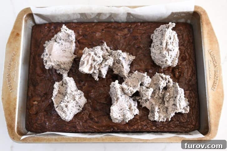 Baked pan of brownies with Oreo frosting dolloped on top.