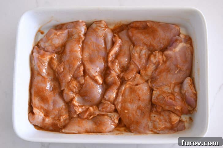 White pan with raw chicken thighs in smoky honey marinade.