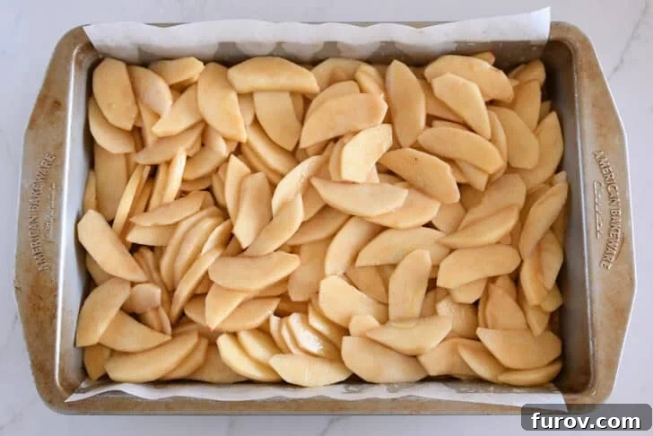Metal 9X13-inch pan filled with sliced apples mixed with caramel and cinnamon.