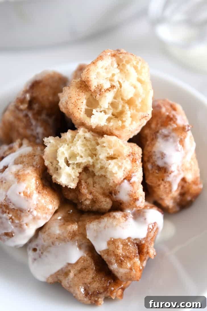 Fluffy Cinnamon Roll Bites Recipe: Soft, Bite-Sized Treats 9 White plate with five cinnamon roll bites drizzled with icing with top cinnamon roll bite in half.