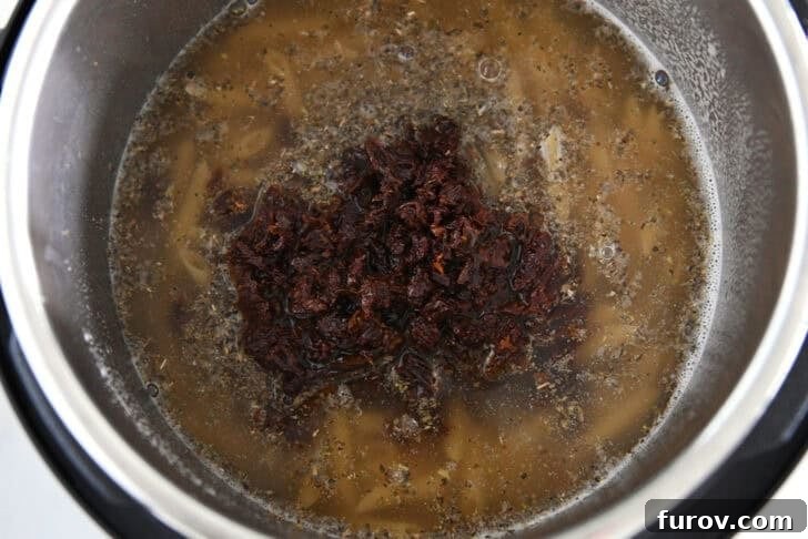 Instant pot with sun-dried tomatoes, broth, seasonings and pasta.