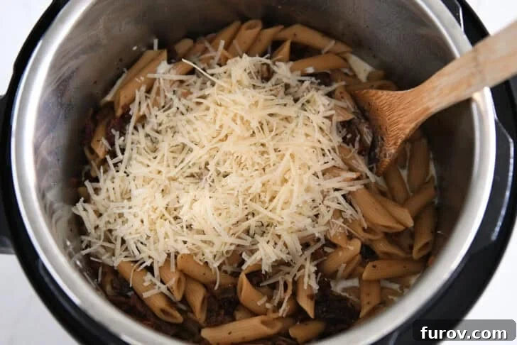 Shredded Parmesan cheese in Instant Pot with cooked pasta, cream and sun-dried tomatoes.